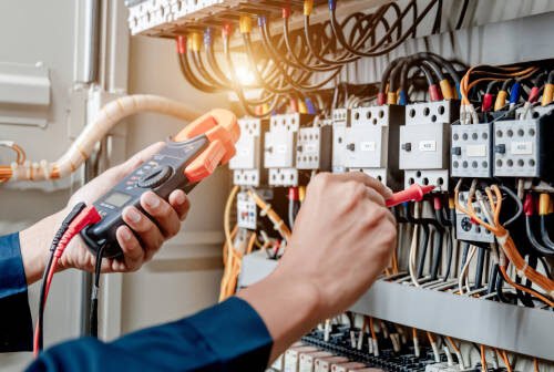 Electrician engineer uses a multimeter to test the electrical installation and power line current in an electrical system control cabinet.