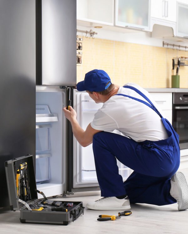 Male technician with screwdriver repairing refrigerator in kitchen